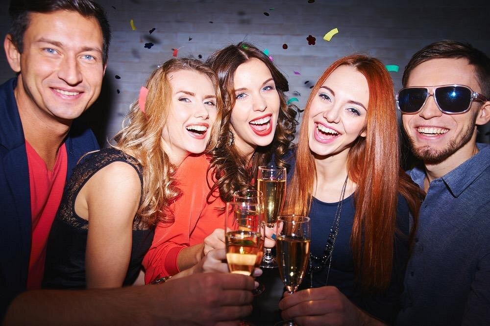 Five young adults with champagne glasses celebrating on a luxury party bus in Las Vegas with neon lights