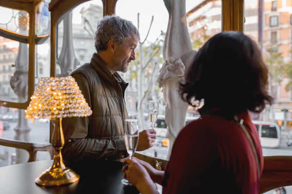 A couple enjoying a glass of cava inside Casa Batllo at night with golden evening lighting illuminating Gaudi's organic architecture