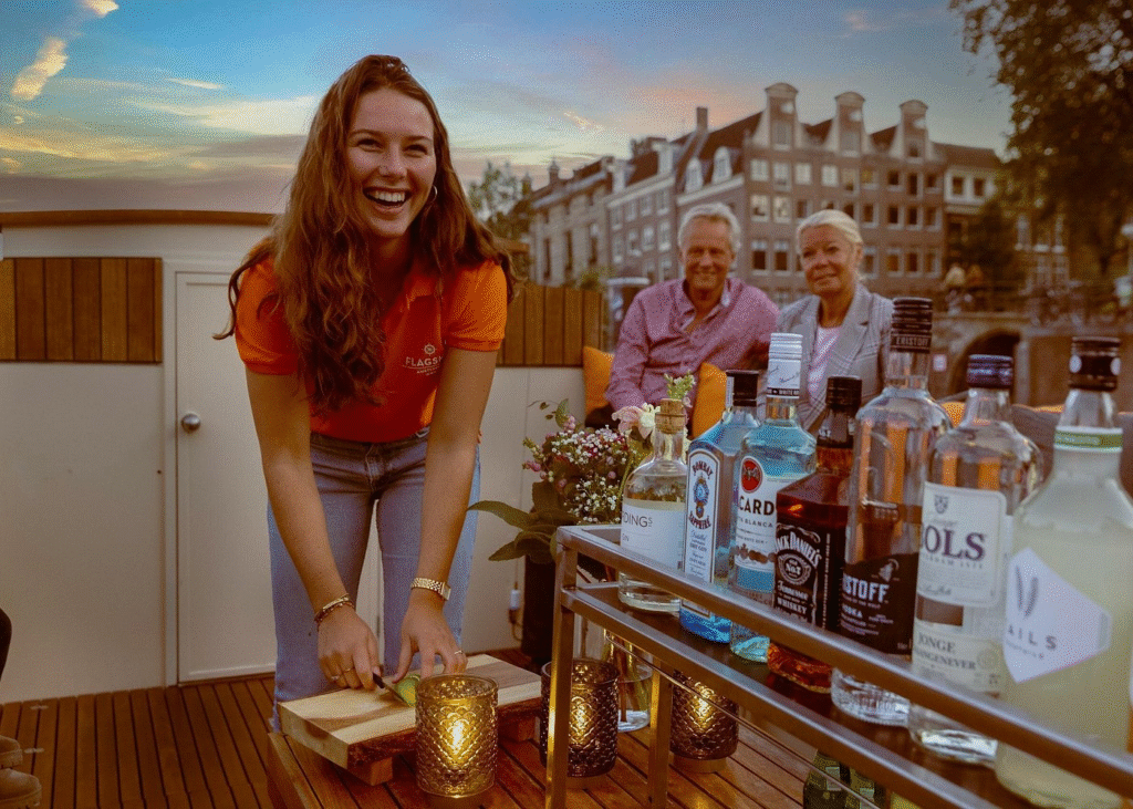 Attractive young woman with her parents relaxing and enjoying drinks on an amsterdam evening canal cruise as historic gabled houses glow in golden twilight