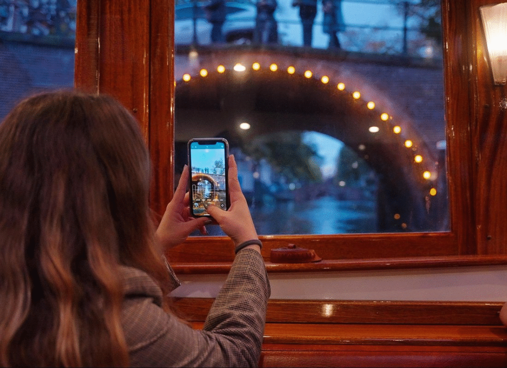 Elegant passengers sipping cocktails and taking great evening photos on a luxury amsterdam evening canal cruise boat with floor-to-ceiling windows and premium seating