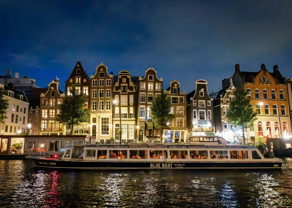 Traditional glass-topped canal boat filled with passengers enjoying classic amsterdam evening canal cruise past illuminated merchant houses