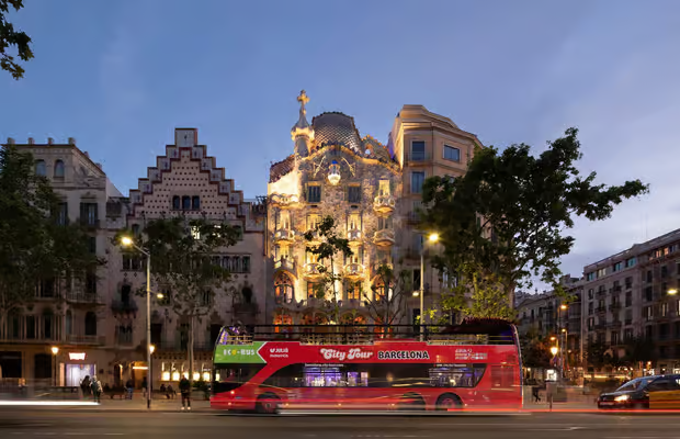 Evening hop on hop off Barcelona night bus with illuminated Sagrada Familia visible in background