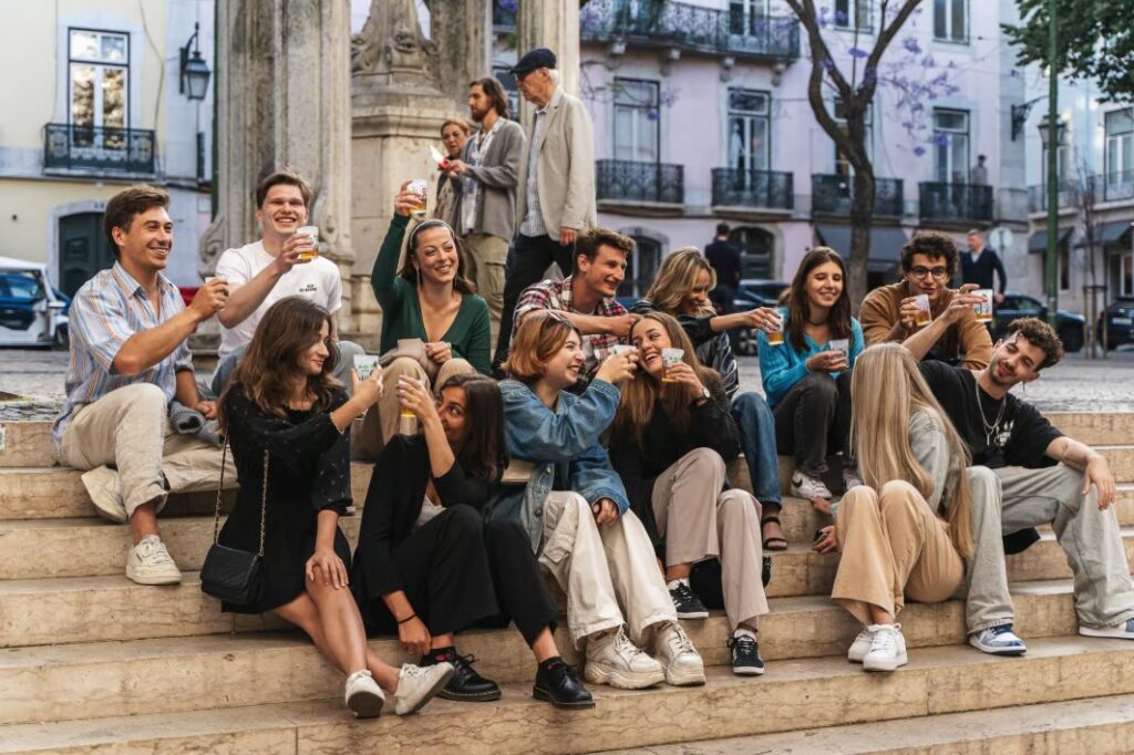 Group of young travelers enjoying drinks and laughing together on a Lisbon pub crawl in Bairro Alto