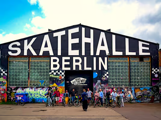 Cyclists stopping at Skatehalle Berlin street art spot during a berlin bike tour with colorful graffiti murals.