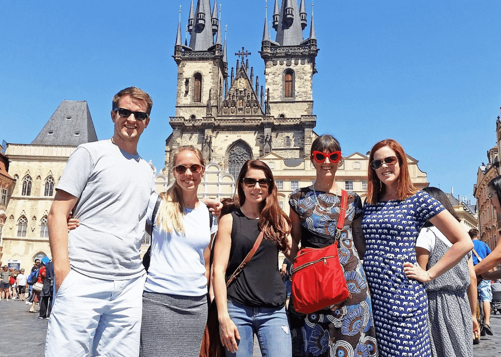 Prague Jewish Quarter walking tour with visitors posing in Old Town Square, featuring the Gothic towers of the Church of Our Lady before Týn in the background