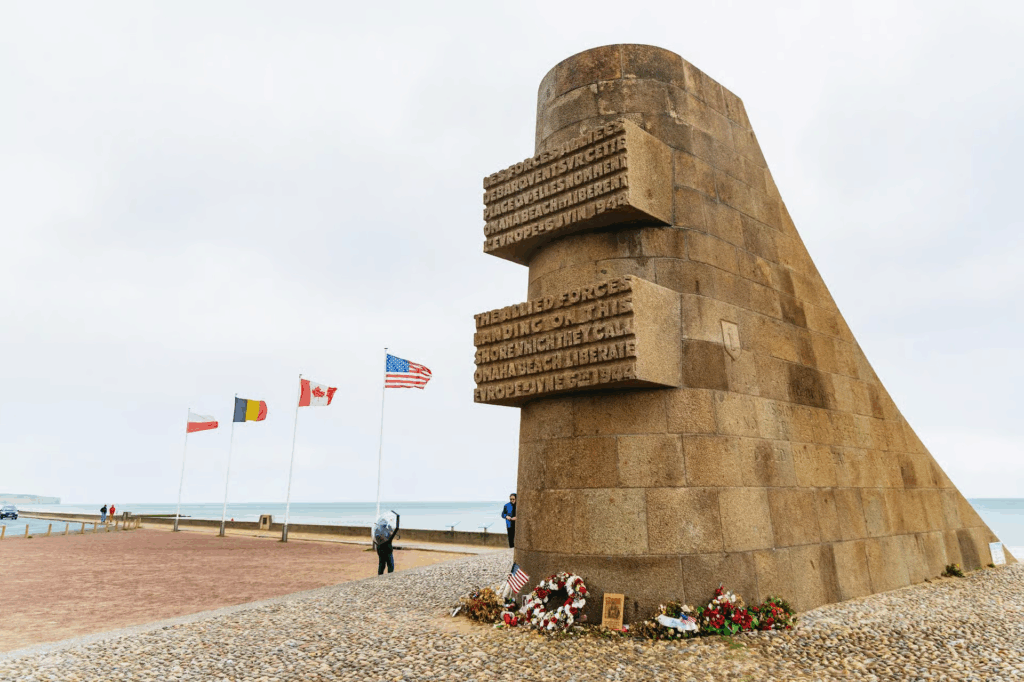 Mont Saint Michel tours showing the Normandy D-Day memorial monument near the coastline with Allied flags flying in the background