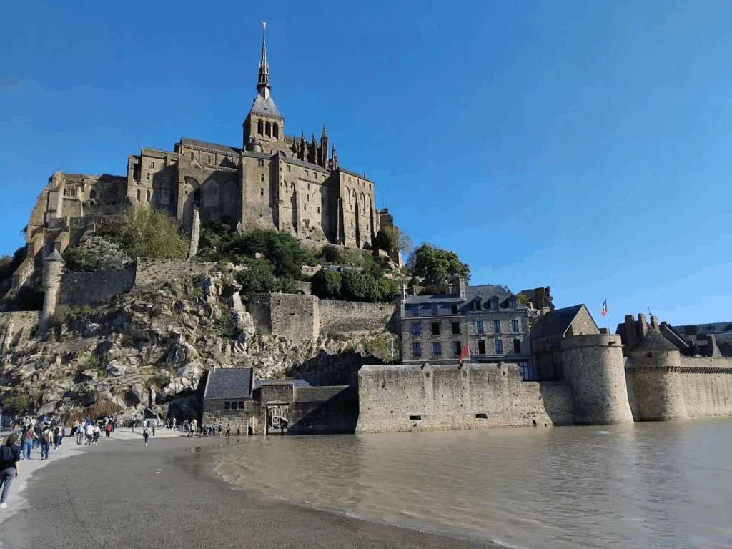 Mont Saint Michel tours showing visitors walking along the tidal causeway with the abbey and fortified walls rising above the shoreline.