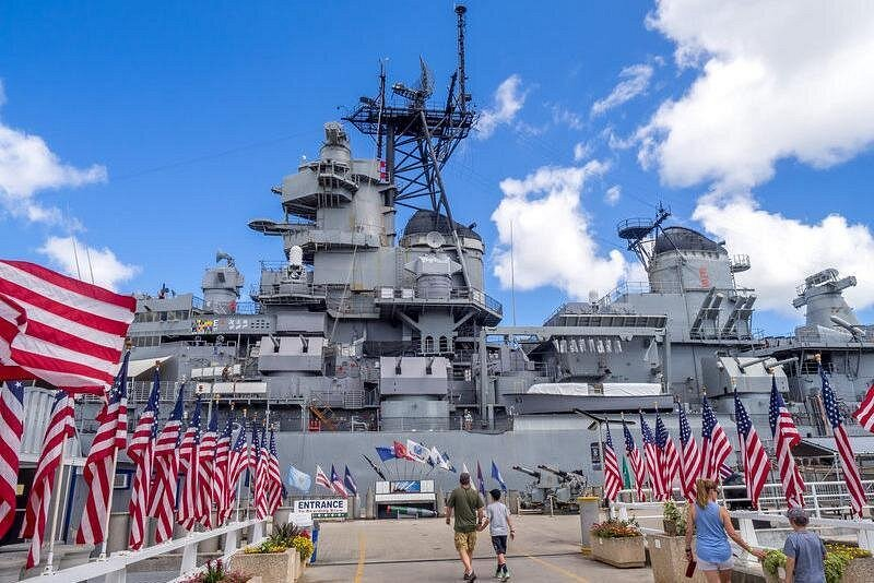 Visitors walking past American flags toward the USS Missouri battleship at Pearl Harbor, a major attraction featured on pearl harbor tours in Honolulu.