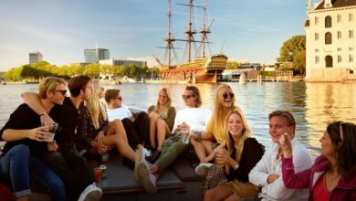 friends enjoying an amsterdam open boat canal cruise with historic ship and waterfront views at sunset